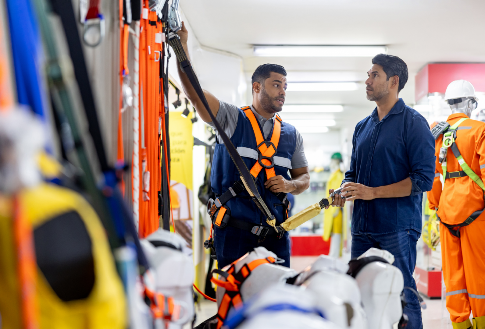 Workers discussing safety harness equipment in store.