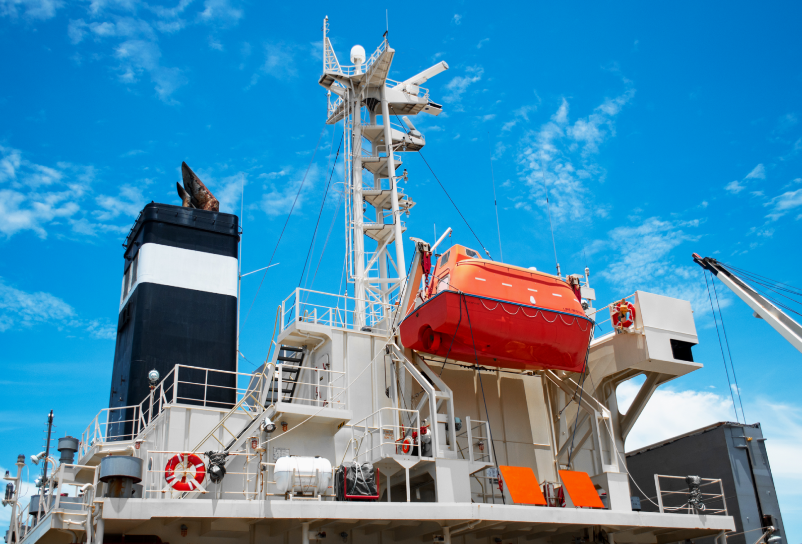 Ship deck with lifeboat and blue sky.